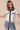 Woman wearing a white blouse with black accents and blue jeans on a beige background