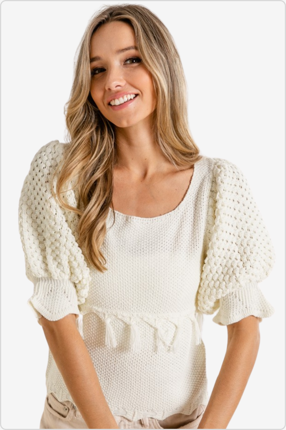 Smiling woman wearing a boho cream knit sweater with fringe trim 
