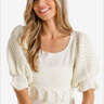 Smiling woman wearing a boho cream knit sweater with fringe trim 