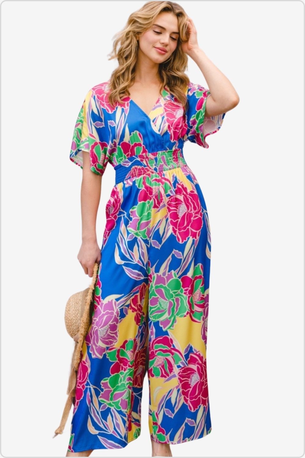 Woman in vibrant floral smocked jumpsuit with a tied back, perfect for a breezy summer day.