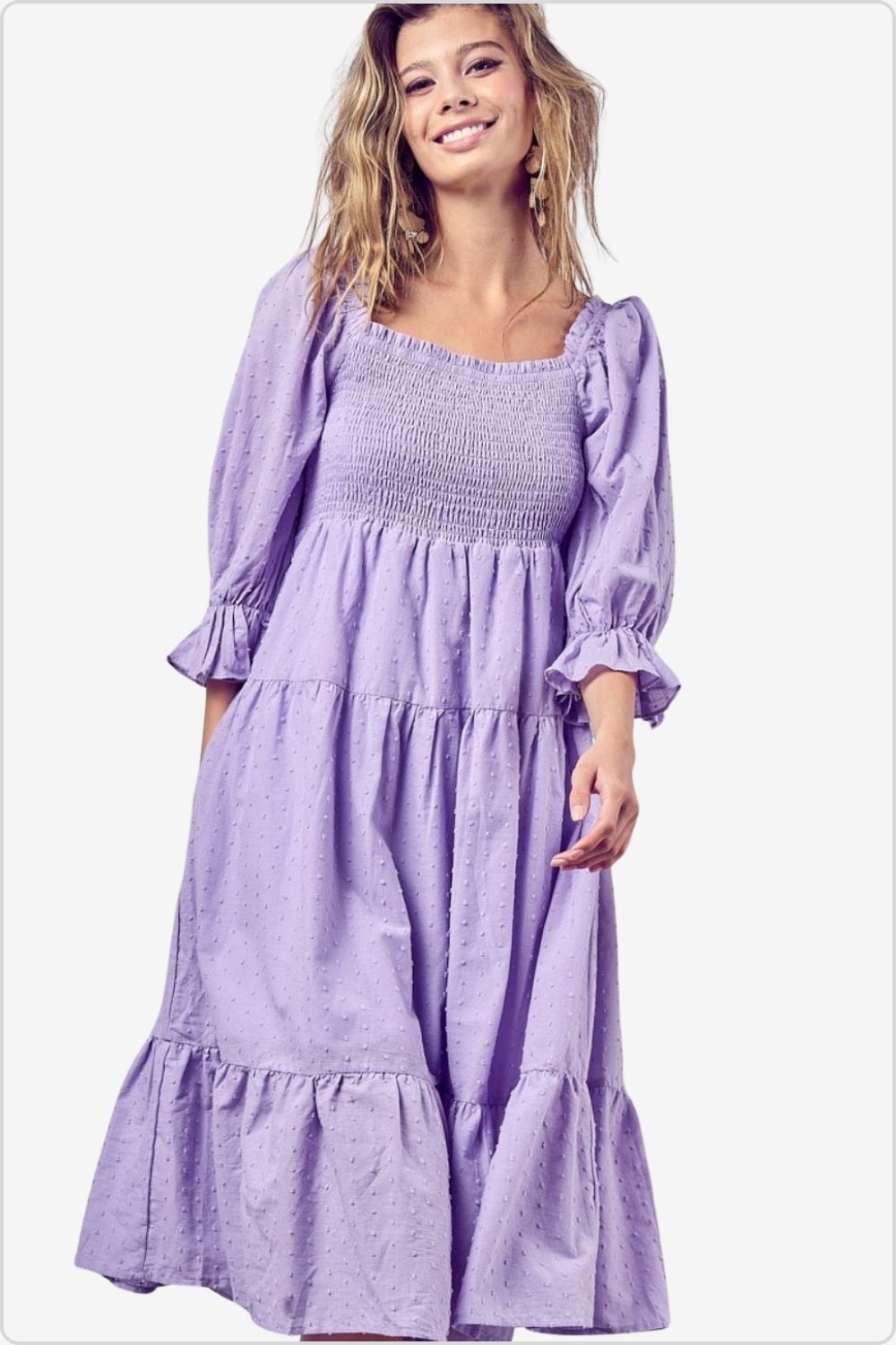 Smiling woman in a lilac swiss dot dress with flounce sleeves and tiered design.