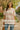 Woman in a pink and white oversized striped polo sweater walking on a sunny street with blooming spring trees.