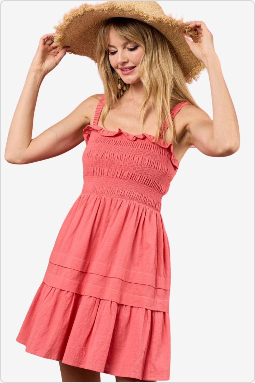 Cheerful woman in a coral smocked mini dress with ruffle hem and straw hat.