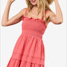 Cheerful woman in a coral smocked mini dress with ruffle hem and straw hat.