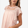 Woman in a soft pink blouse with delicate lace detailing and flutter sleeves.