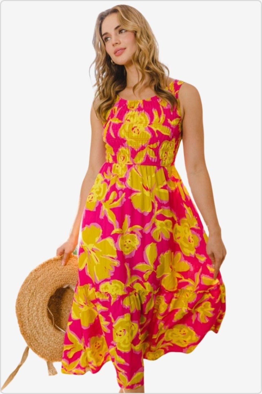 Woman with straw hat posing in a pink and yellow floral smocked ruffled midi dress.