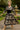 Woman twirling in abstract floral print midi dress with gold heels, fountain background, sunny park.
