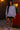 Woman in a light purple sweatshirt and black shorts standing in front of a red vintage vending machine.