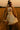 Walking through wheat field in flag sweater with tiered cream skirt, teddy coat, cowboy boots, sunset glow
