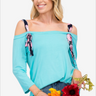 Radiant woman in aqua blue off-shoulder top with floral straps, fresh and summery style.