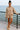 Smiling woman standing seaside in ash mocha fleece sweatshirt and shorts set with slip-ons, railing view.