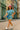 Model in acid washed tee and shorts with pink cap, blue bag, and white sneakers