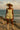 Model in sage jacquard set styled with cream cowboy boots and wide-brim hat by the ocean