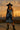 Model in pinstripe mini dress with belt, black cowboy boots, and hat on rooftop at sunset