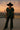 Teal satin blouse styled with black leather pants, wide hat, and heeled boots at sunset