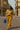 Model wearing striped oversized shirt with yellow trousers, green scarf, and colorful heels
