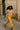 Sweater top styled with yellow pants, sandals, and hat for sunny streetwear style
