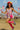 Model jumping in ribbon top with matching shorts, pink socks, and rainbow sandals