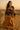 Woman in a patterned t-shirt and long skirt standing in a desert landscape at sunset.