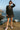 Woman in black babydoll dress with polka dots, plaid trim, tiered hem, standing on canyon edge, sunset glow