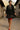Woman walking in polka dot plaid trim babydoll dress, red biker shorts, red flats, stone village street, mountains
