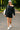Woman in black outfit with white cap and backpack walking on a paved path in a park.