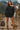 Woman standing on a mountain path with a decorated llama, holding a handbag.
