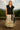 Smiling in black sweater vest with floral embroidered skirt and boots, mountain terrace, clear sky