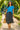 Walking through garden in blue ribbed tee with floral skirt and straw sandals, sunny midday light