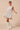 Model wearing ivory mini dress with bow pattern and sleeveless shape