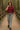 Fashion model walking in merlot colorblock scallop shirt with gray denim, forest bridge, soft light.