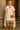 Woman in a classical outfit with a cape and sandals standing in front of stone columns.