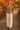 Woman in oatmeal crochet knit cardigan, cream pants and brown loafers, standing on wooden bridge, autumn trees