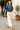 Woman wearing a blue shirt and white pants walking outdoors.