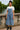 Woman posing on stone bridge in denim wide leg overalls with white blouse, riverside morning.