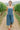 Woman strolling vineyard path in denim wide leg overalls with red flats and white tank, daylight.