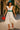 White tiered dress with teal hat and red sandals styled for summer strolls in the city