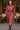 Woman walking past Parisian cafe in dusty rose textured midi dress with black belt, cowboy boots, holding coffee