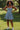 Woman wearing fit and flare denim mini dress with white sneakers, standing on grass in sunny park, smiling.