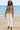 Woman in floral blouse and white jeans standing barefoot on sandy beach