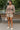 Woman in floral blouse and beige shorts with cream loafers near park fountain