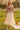 Woman in floral blouse and cream tiered skirt holding woven bag in spring park