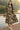 Woman in a floral dress standing on a wooden deck by a body of water.