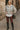 Woman in heather gray jacquard zip jacket, burgundy leggings, black boots, olive bag, city street background