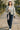 Woman in heather gray jacquard zip jacket, jeans, white sneakers, white cap, walking in Kyoto park