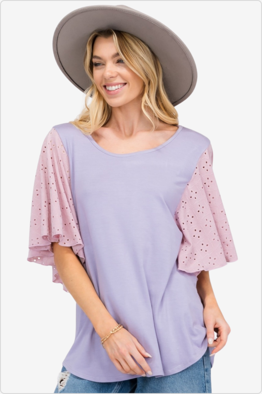 Joyful woman in lavender blouse with pink eyelet sleeves and a wide-brim hat, stylish summer look.