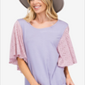 Joyful woman in lavender blouse with pink eyelet sleeves and a wide-brim hat, stylish summer look.