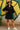 Woman in a black dress and white sneakers standing in front of a colorful wall.
