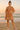 Woman in rust embroidered mini dress with tassel neckline and puff sleeves, standing on a sandy beach at sunrise in pink sneakers