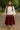 Woman walking in oatmeal linen drawstring top with red midi skirt and scarf, park path.
